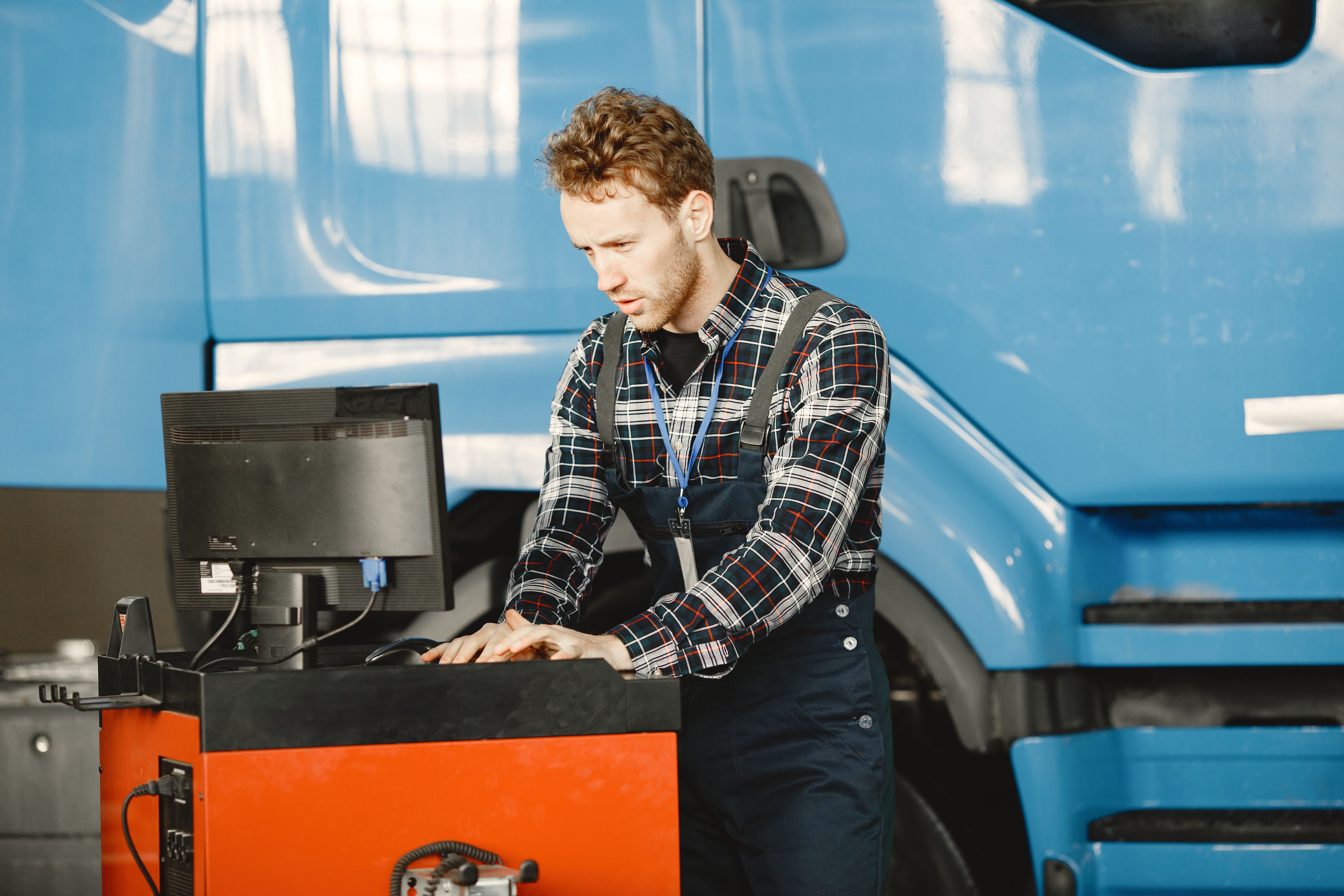 Truck technician using a diagnostic computer beside a blue commercial truck in a service bay