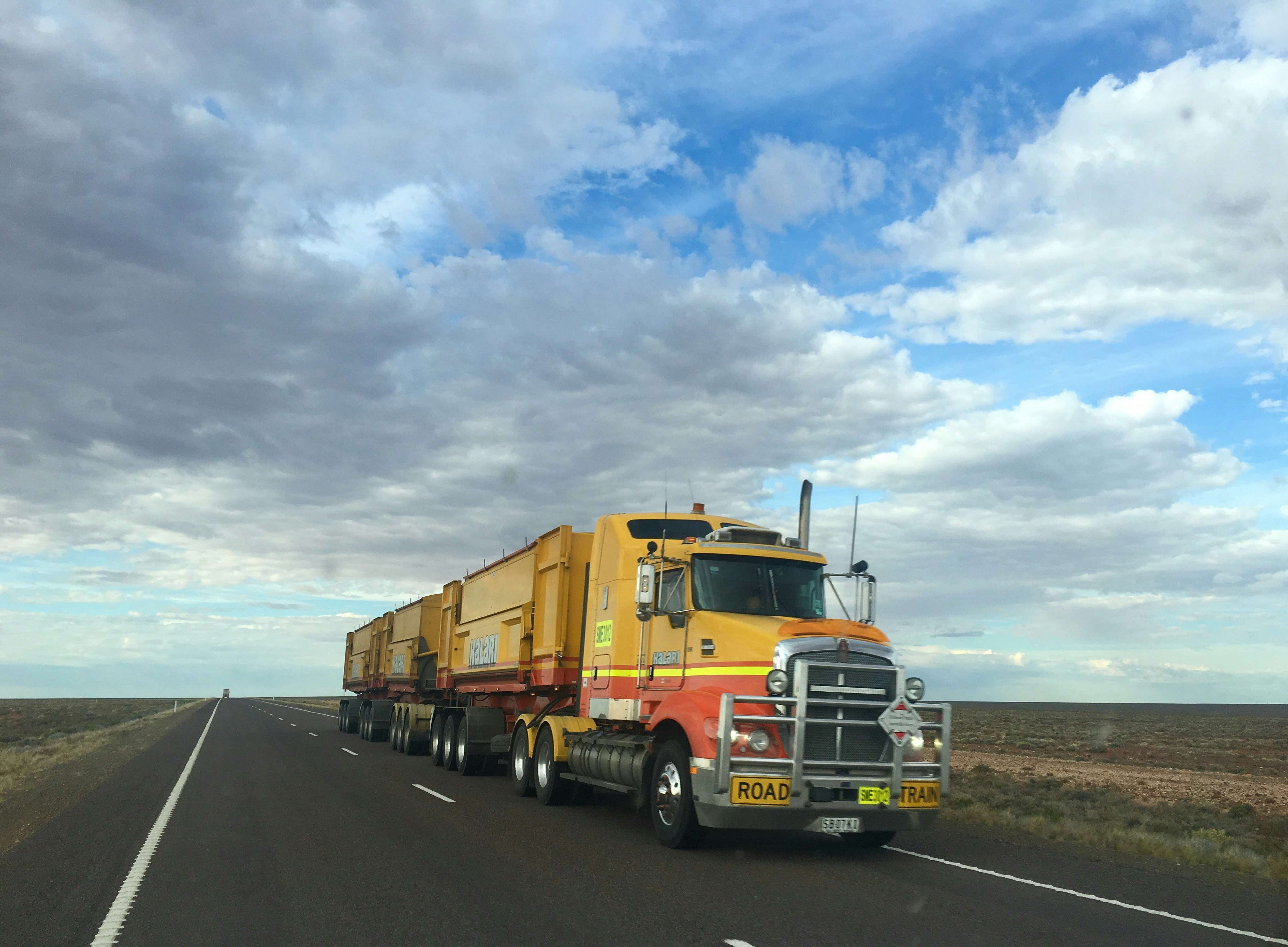 Long-haul truck hauling multiple trailers along an open highway under a cloudy sky